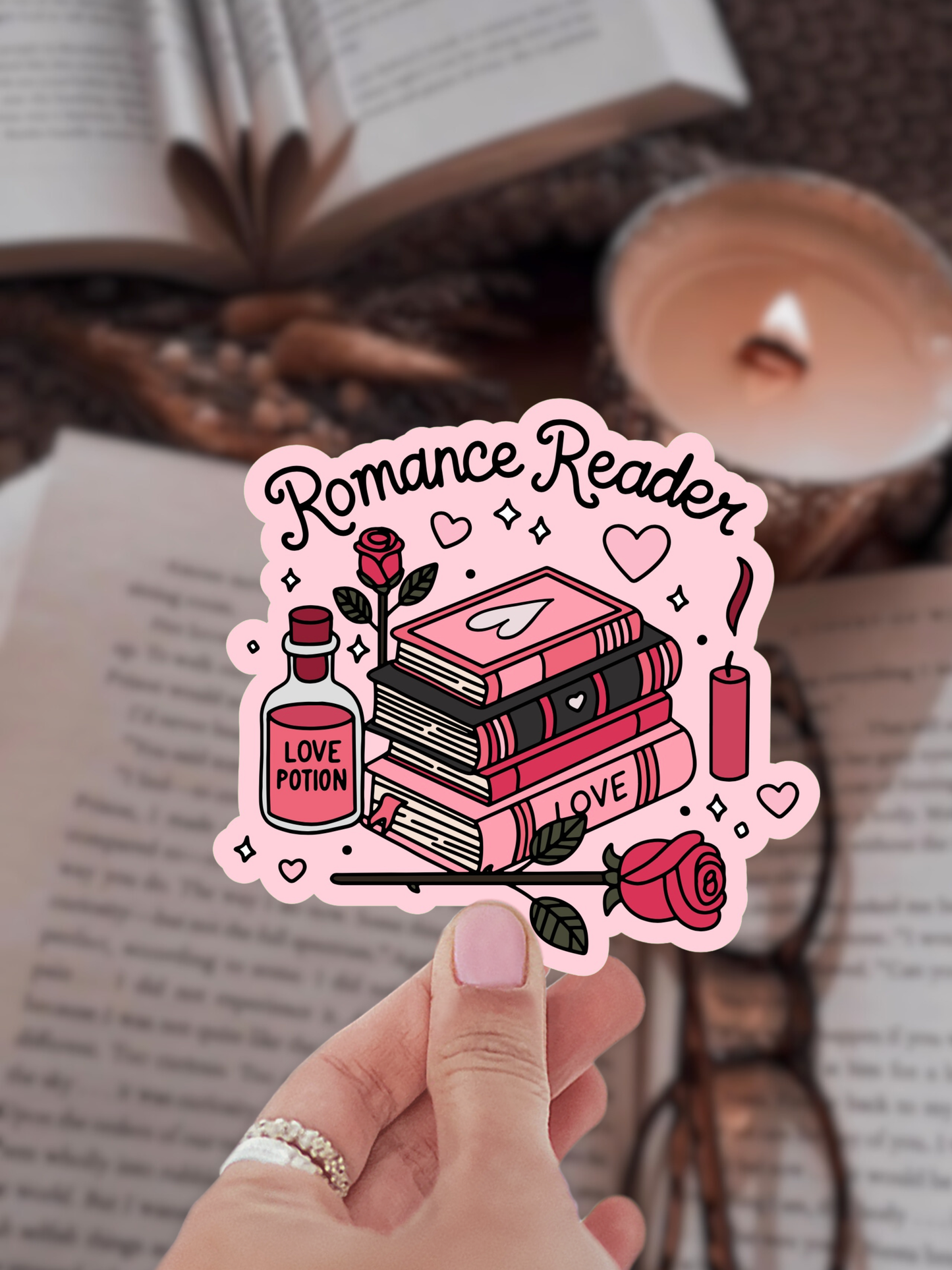 Sticker with 'Romance Reader' design held by a hand, with books and a candle in the background.