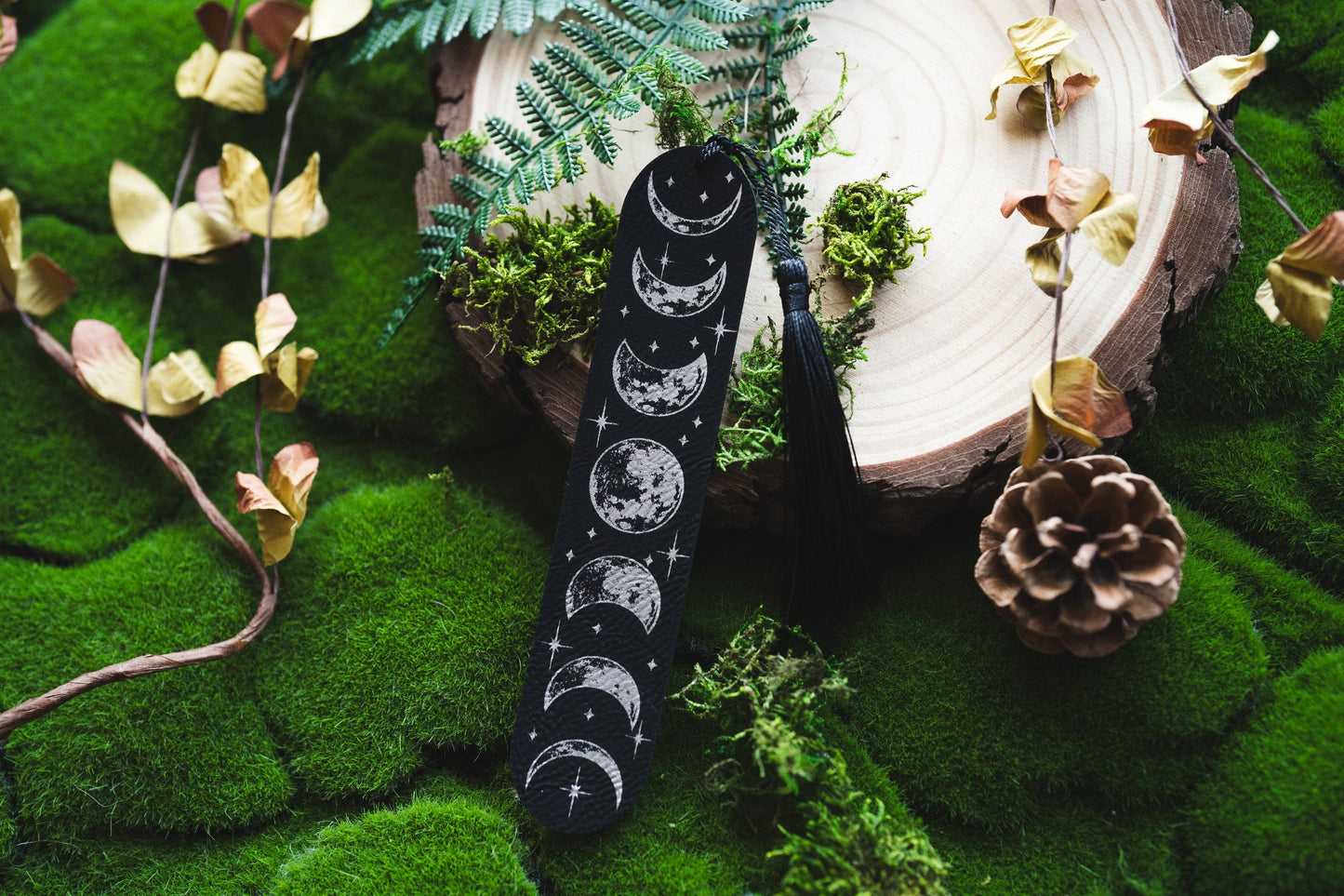 Black sock with moon phases on a green mossy surface with decorative elements