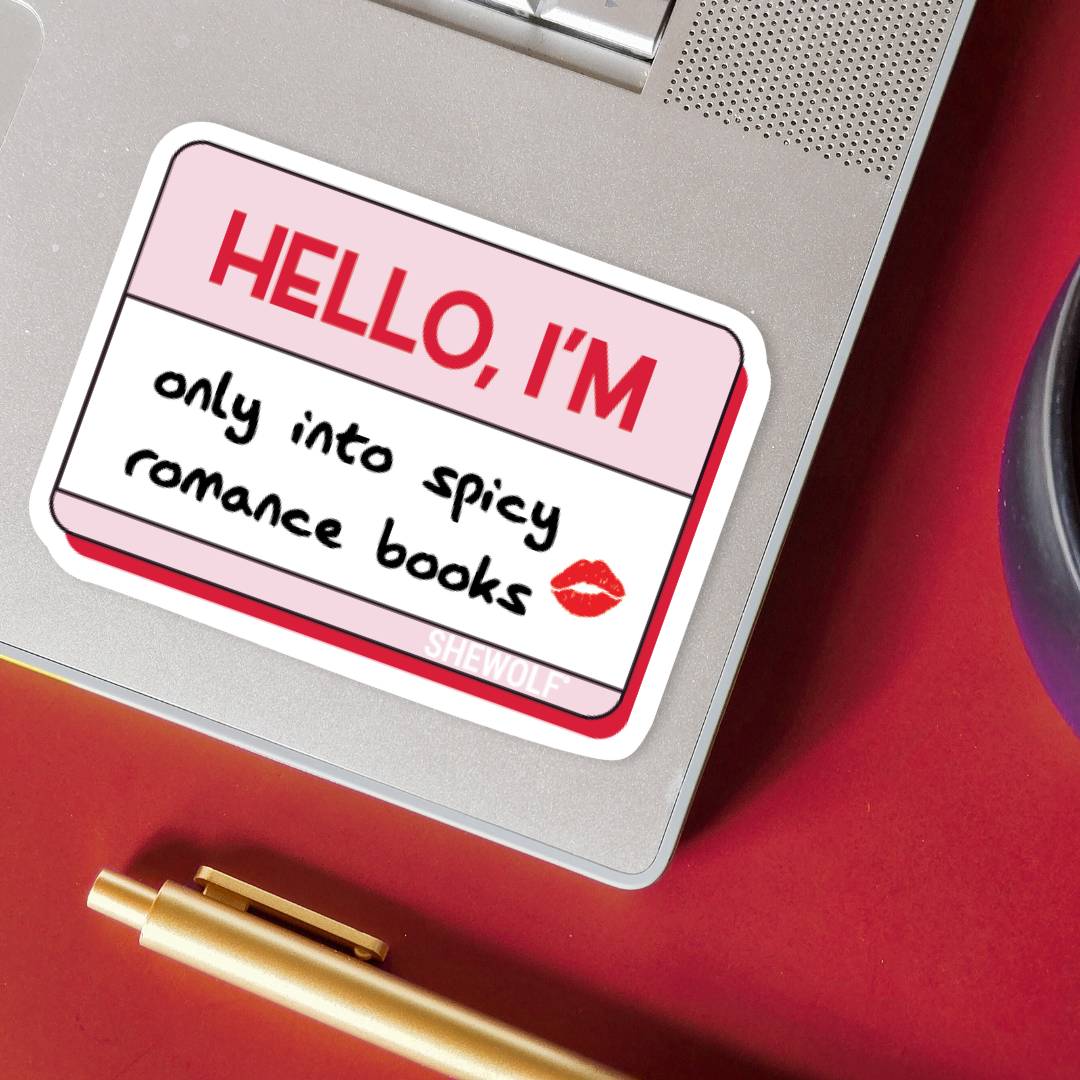 Sticker on a laptop with text 'HELLO, I'M only into spicy romance books' on a red surface.