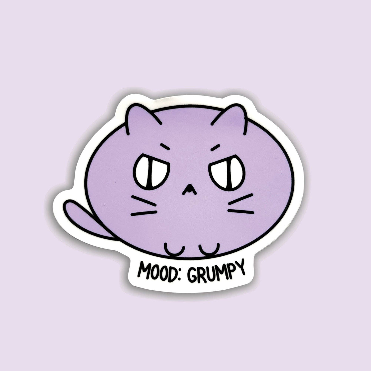 A die-cut sticker featuring a cartoon purple cat with a grumpy expression and the text 'MOOD: GRUMPY' on a light lavender background.