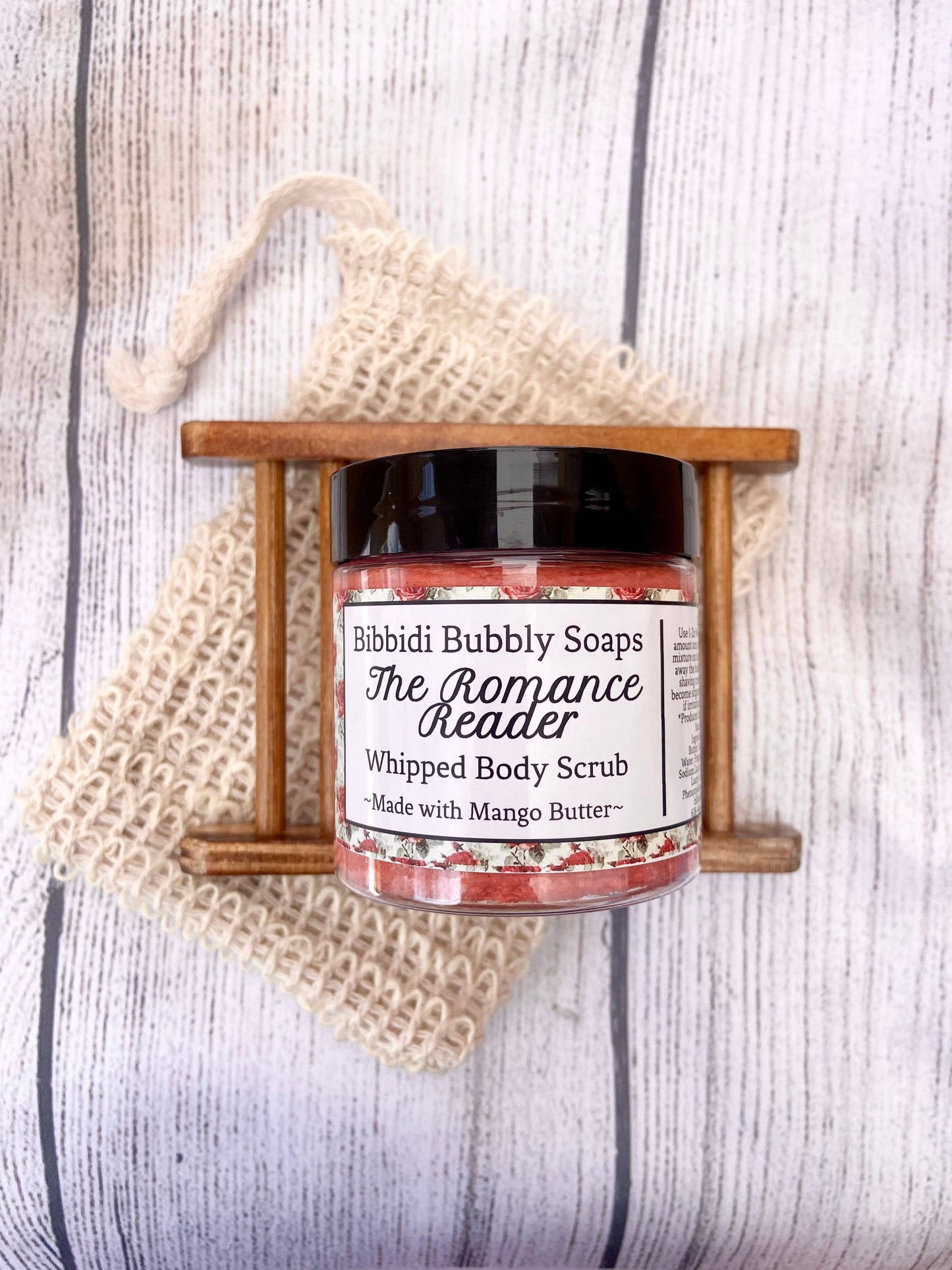Jar of 'The Romance Reader' whipped body scrub by Bibbidi Bubbly Soaps on a wooden stand with a textured background.