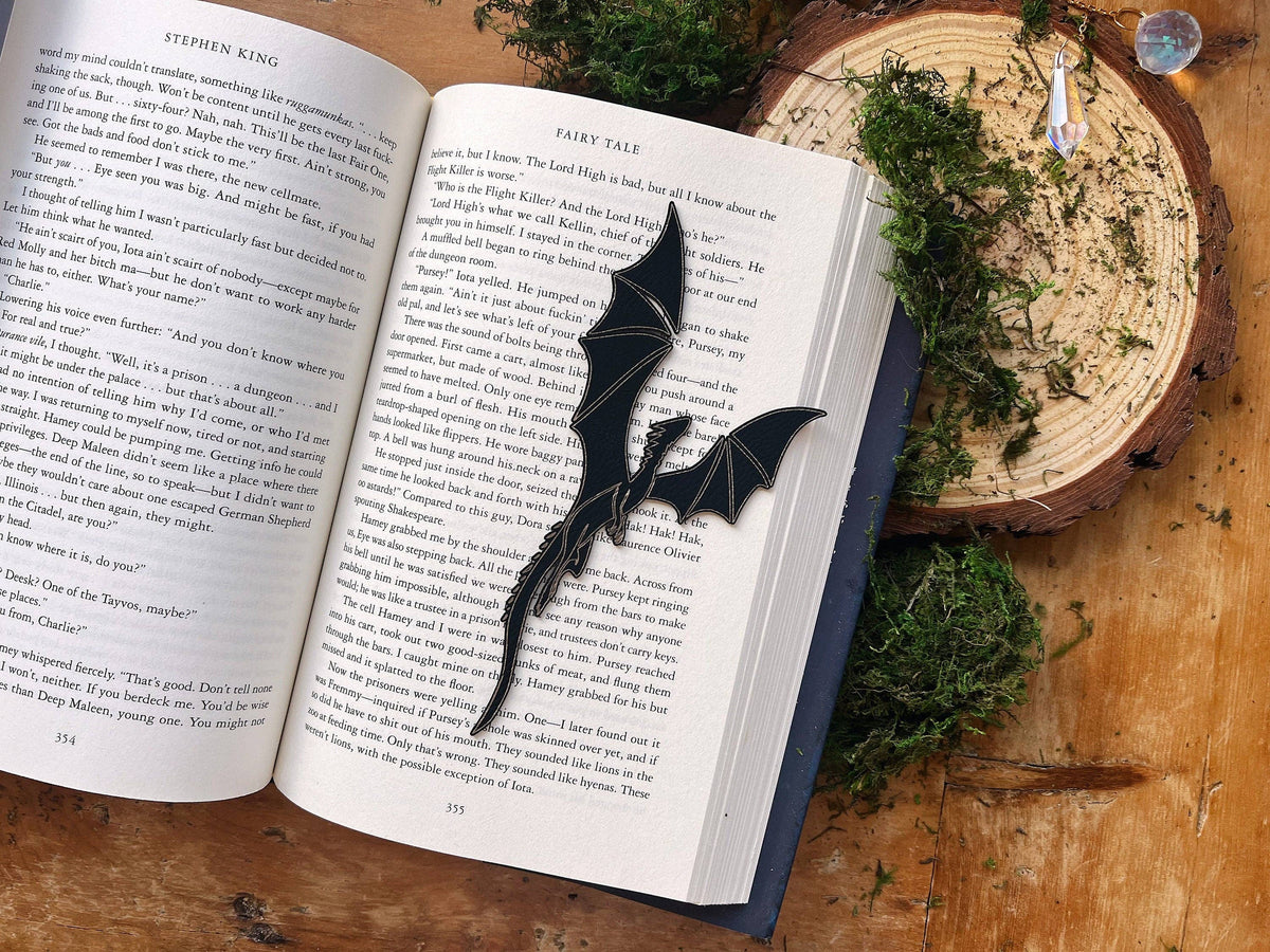 Open book with a dragon-shaped bookmark on a wooden surface with greenery