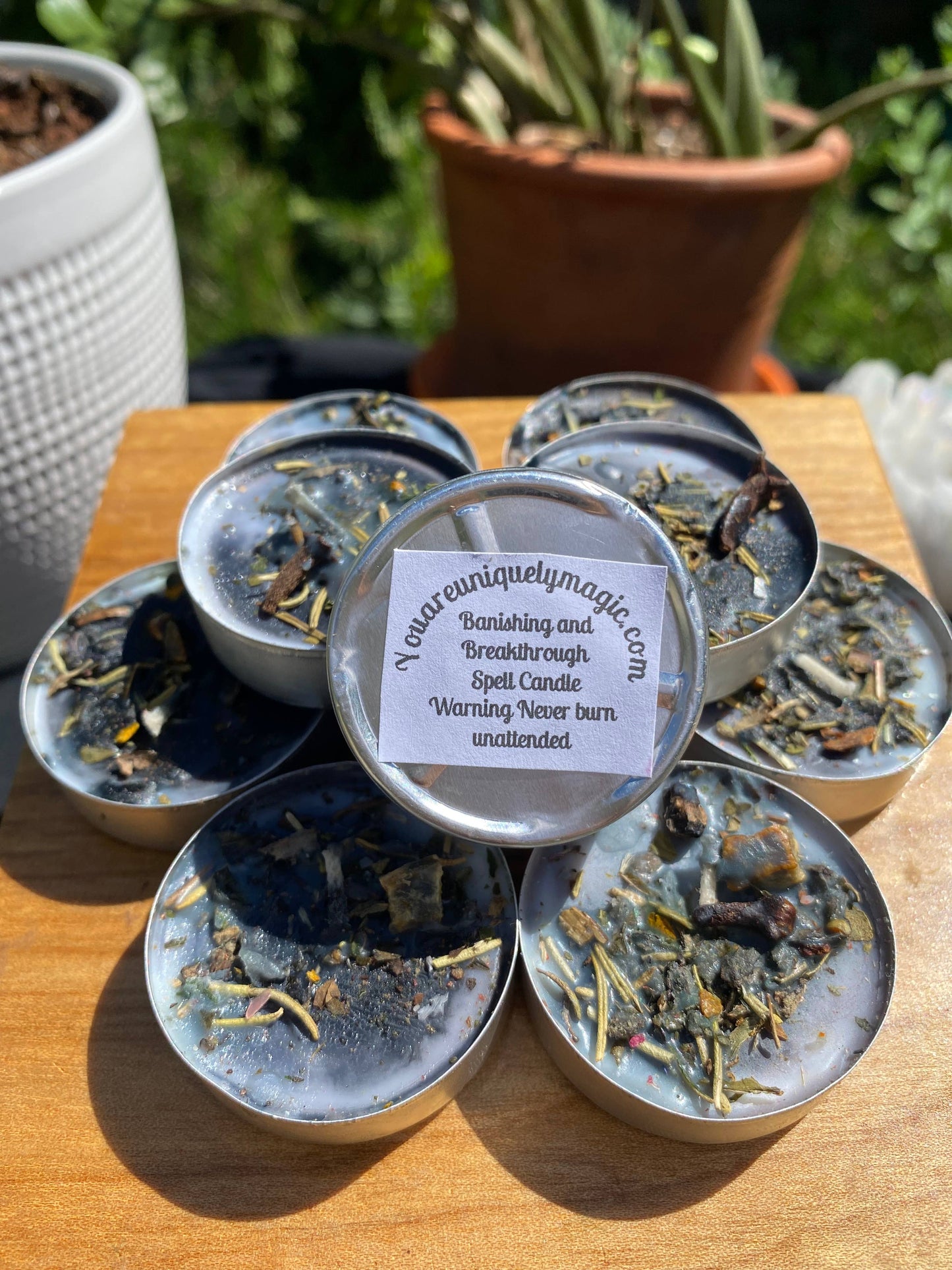 Collection of small candles in tins on a wooden surface with plants in the background.