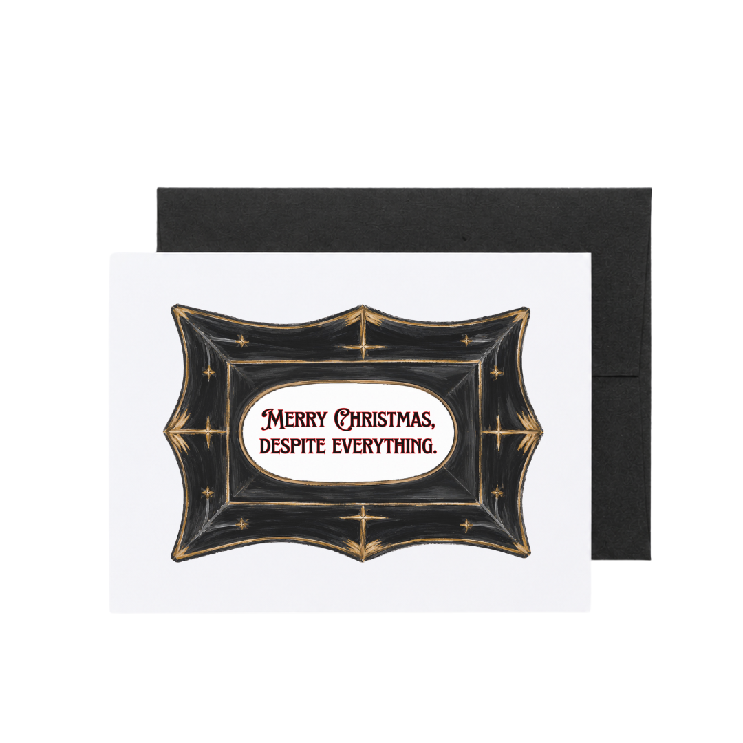 A Christmas greeting card with a black envelope behind it, featuring a decorative black crest with gold stars and the text 'Merry Christmas, Despite Everything.' on a white card.
