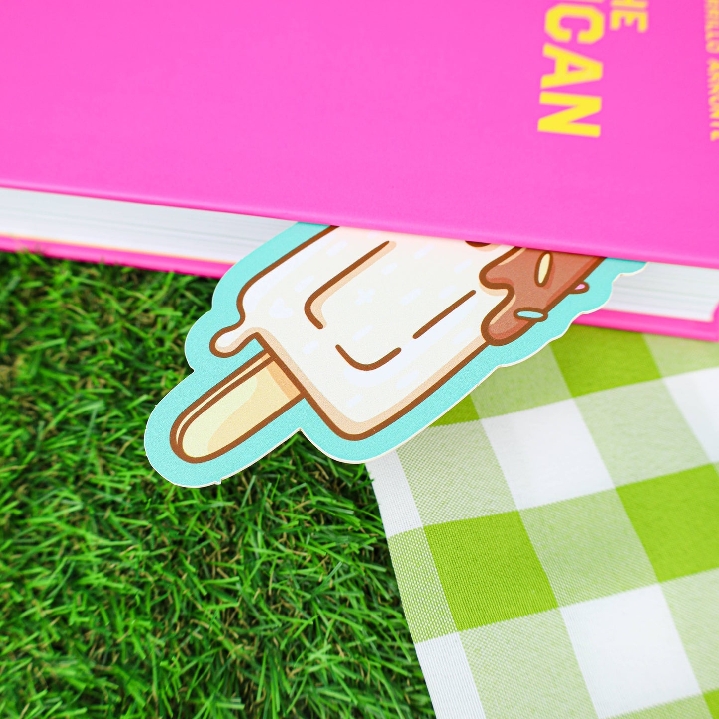 Ice cream-shaped bookmark on a green checkered tablecloth with a pink book in the background.