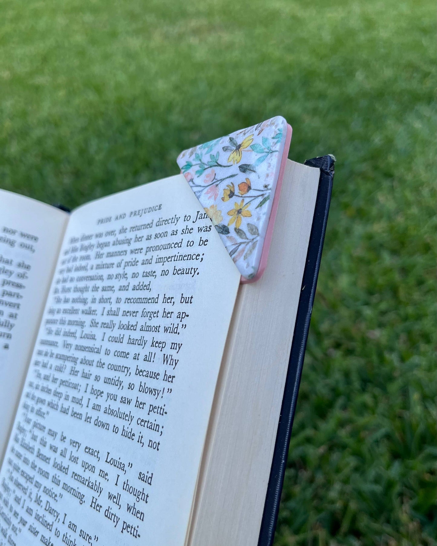 Floral triangle-shaped bookmark on an open book with grass in the background