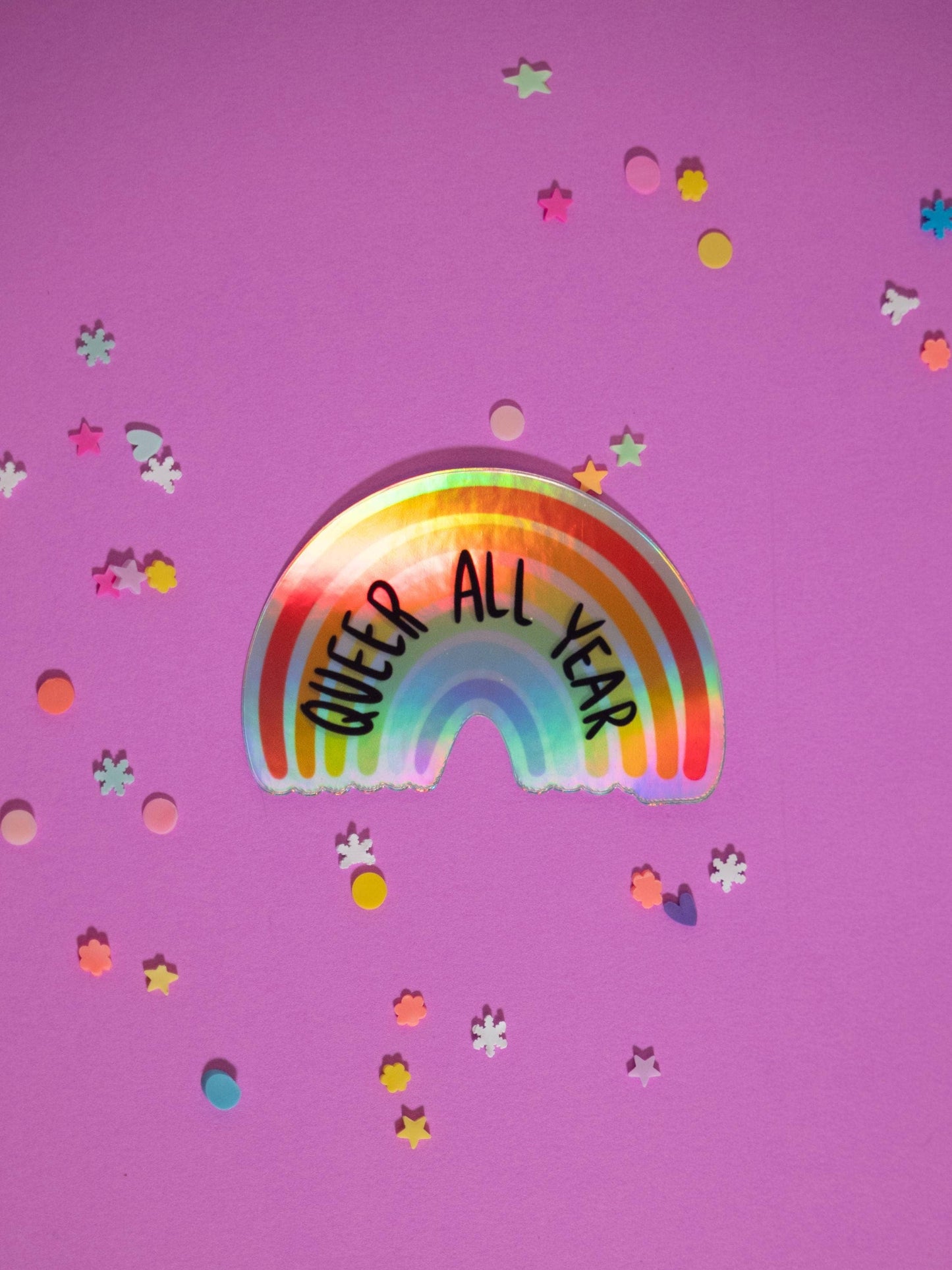 Rainbow sticker with 'QUEER ALL YEAR' text on a purple background with confetti