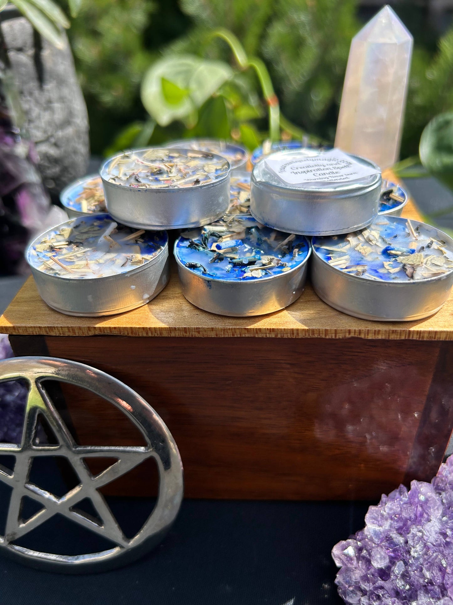 Set of small candles on a wooden surface with crystals and a pentacle symbol in the foreground.