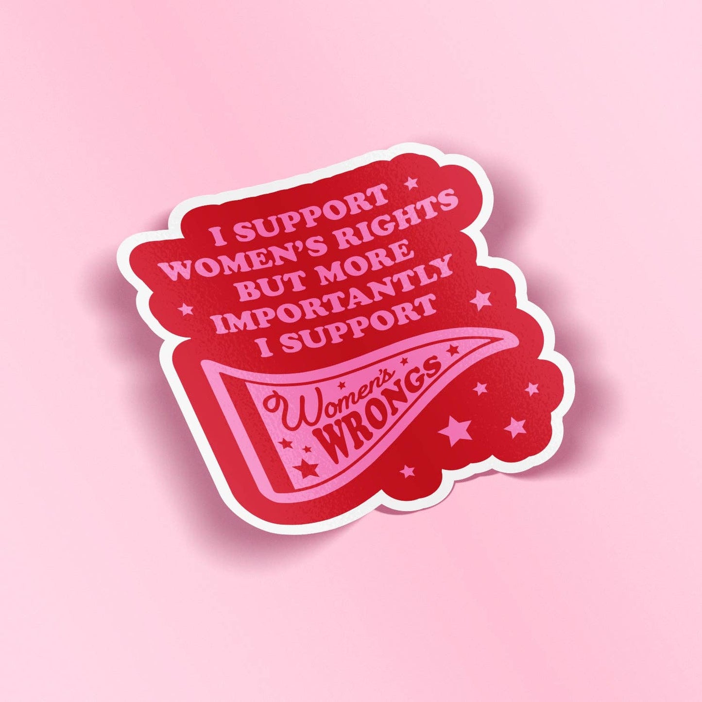 A red die-cut sticker with a white border featuring the text 'I SUPPORT WOMEN'S RIGHTS BUT MORE IMPORTANTLY I SUPPORT Women's Rights WRONGS' and a pennant design, shown on a solid pink background.