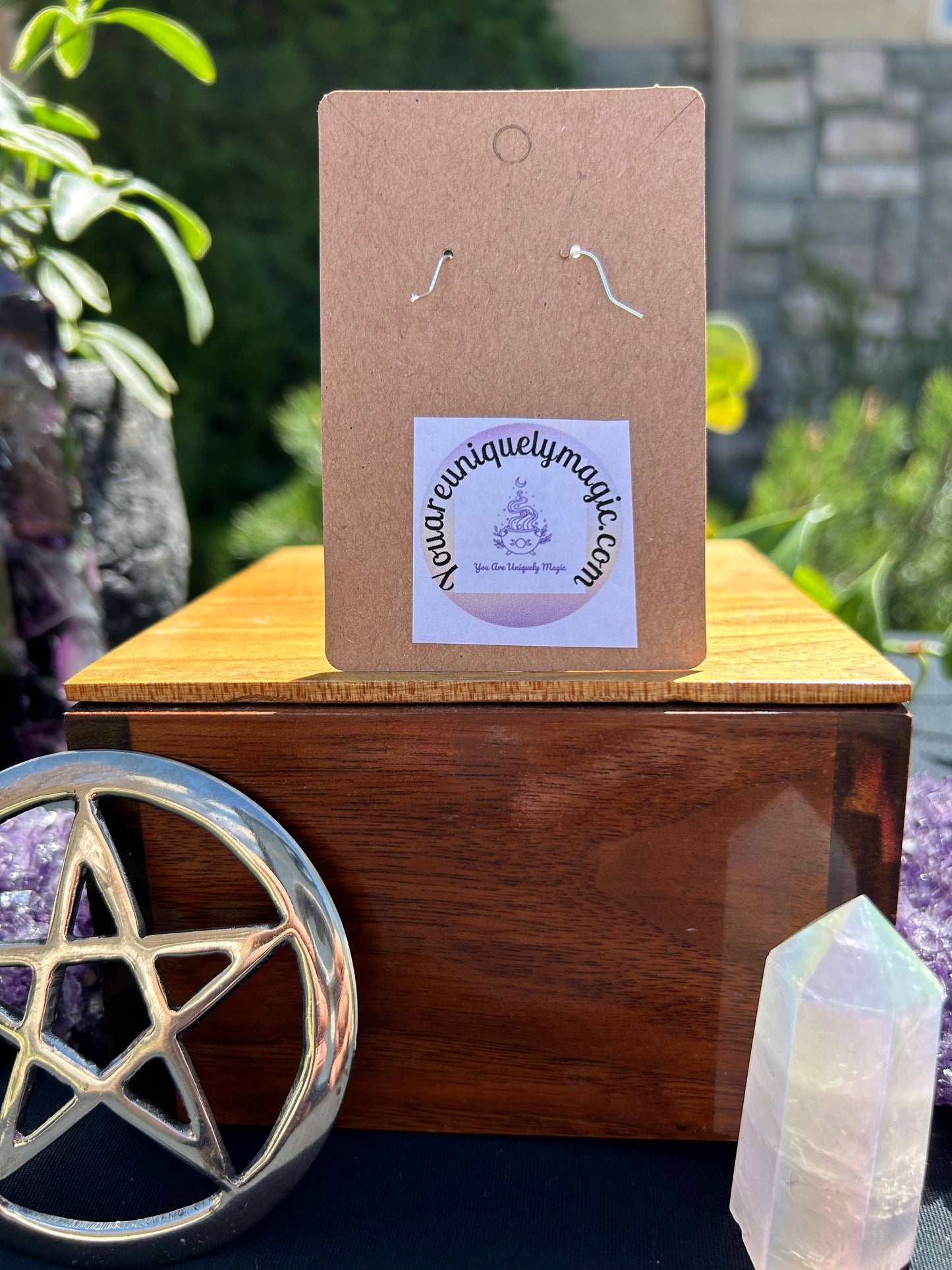 Earring card with a website label on a wooden block with crystals and a pentacle symbol in the background.