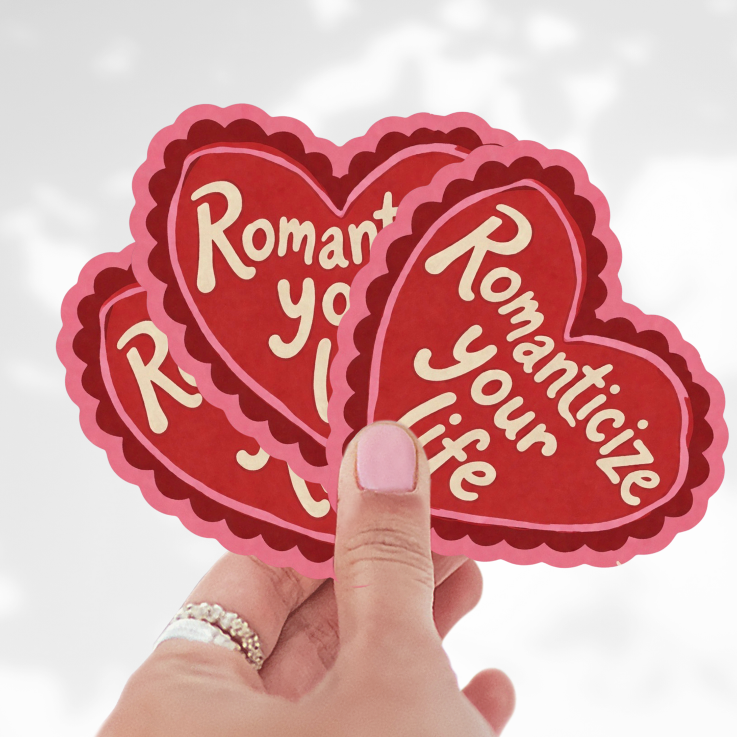 Heart-shaped stickers with 'Romanticize your life' text held by a hand against a light background