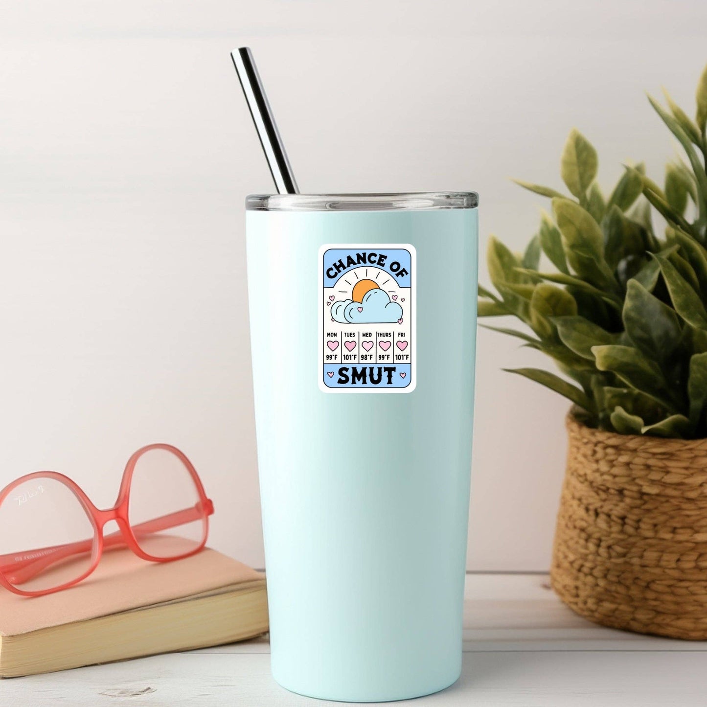 Light blue tumbler with a graphic design on a white surface with a plant and glasses in the background