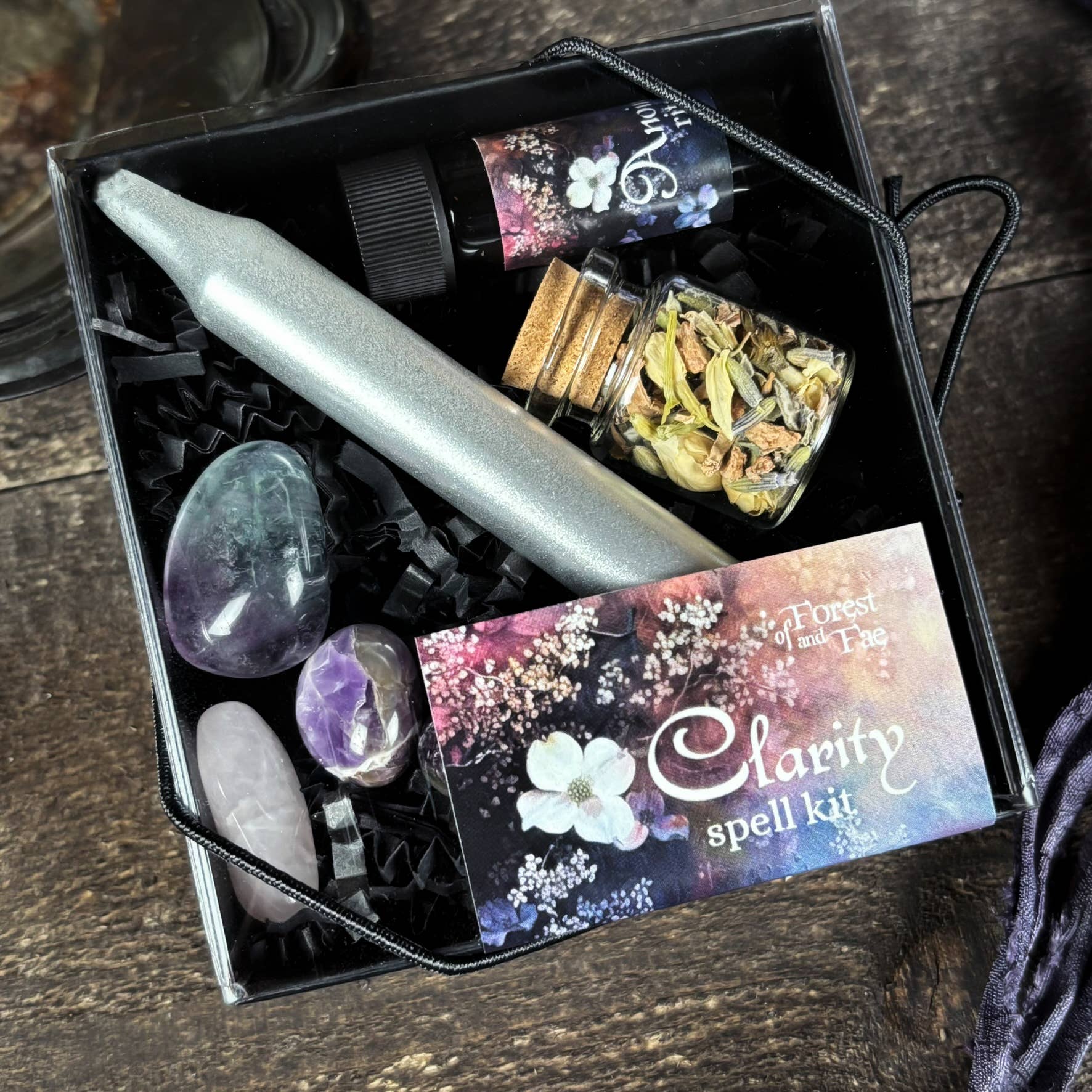 Glamour photo of a 'Clarity spell kit' with crystals, candles, and herbs on a wooden surface.