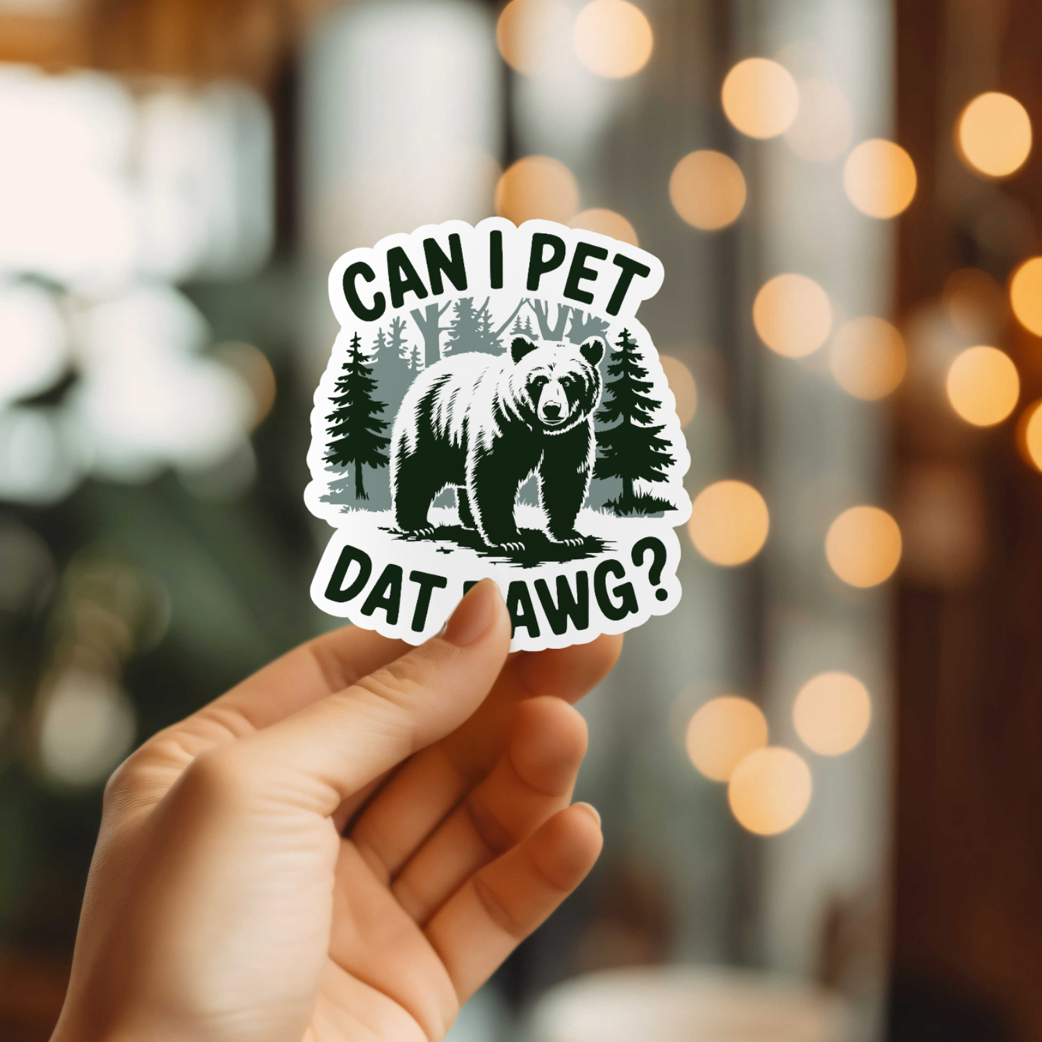 Hand holding a sticker with a bear graphic and text against a blurred background with lights