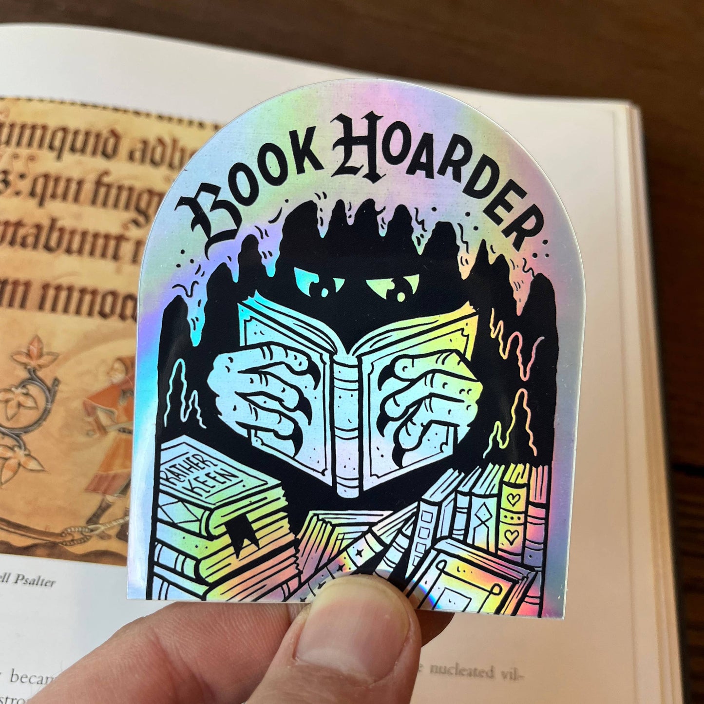 Holographic 'Book Hoarder' sticker held over an open book