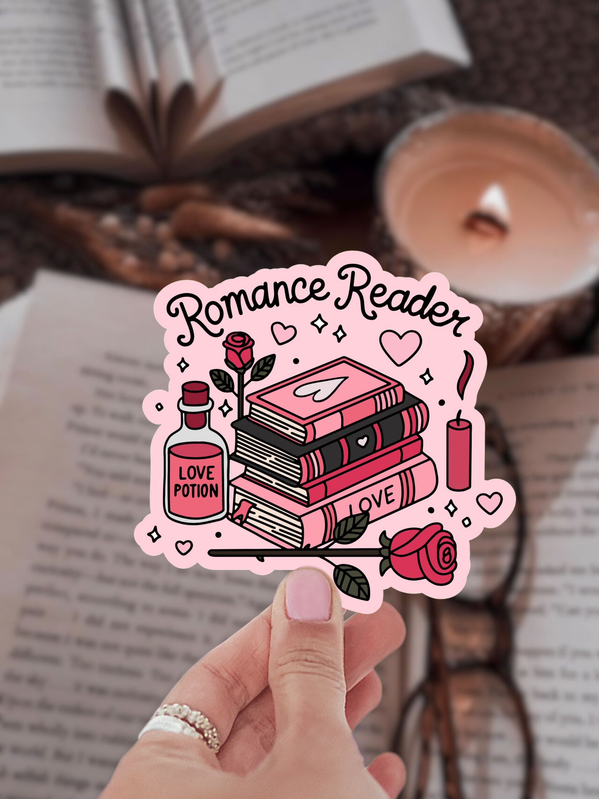 Sticker with 'Romance Reader' design held by a hand, with books and a candle in the background.