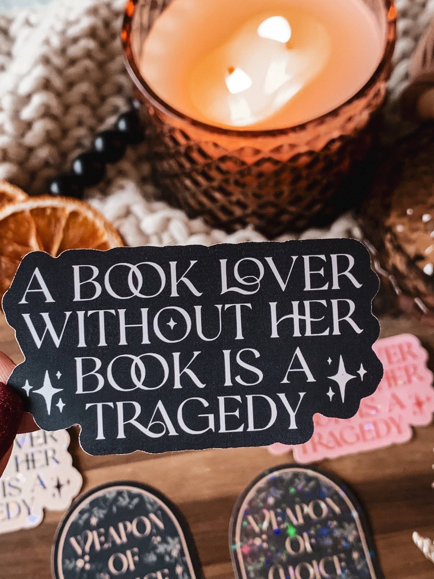 Decorative sign with text 'A book lover without her book is a tragedy' next to a lit candle.