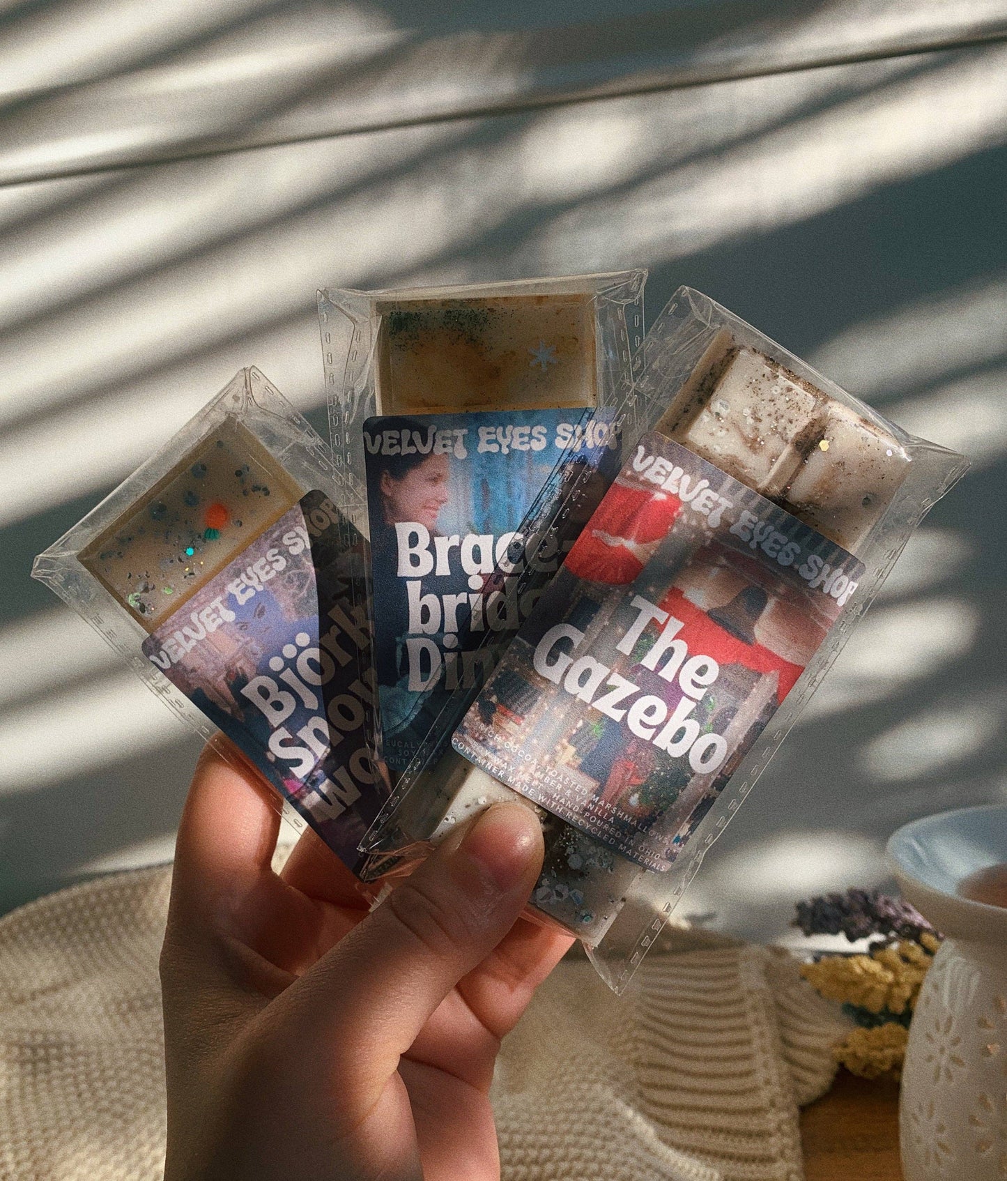 Hand holding four transparent plastic packages with printed text and images on a light background.