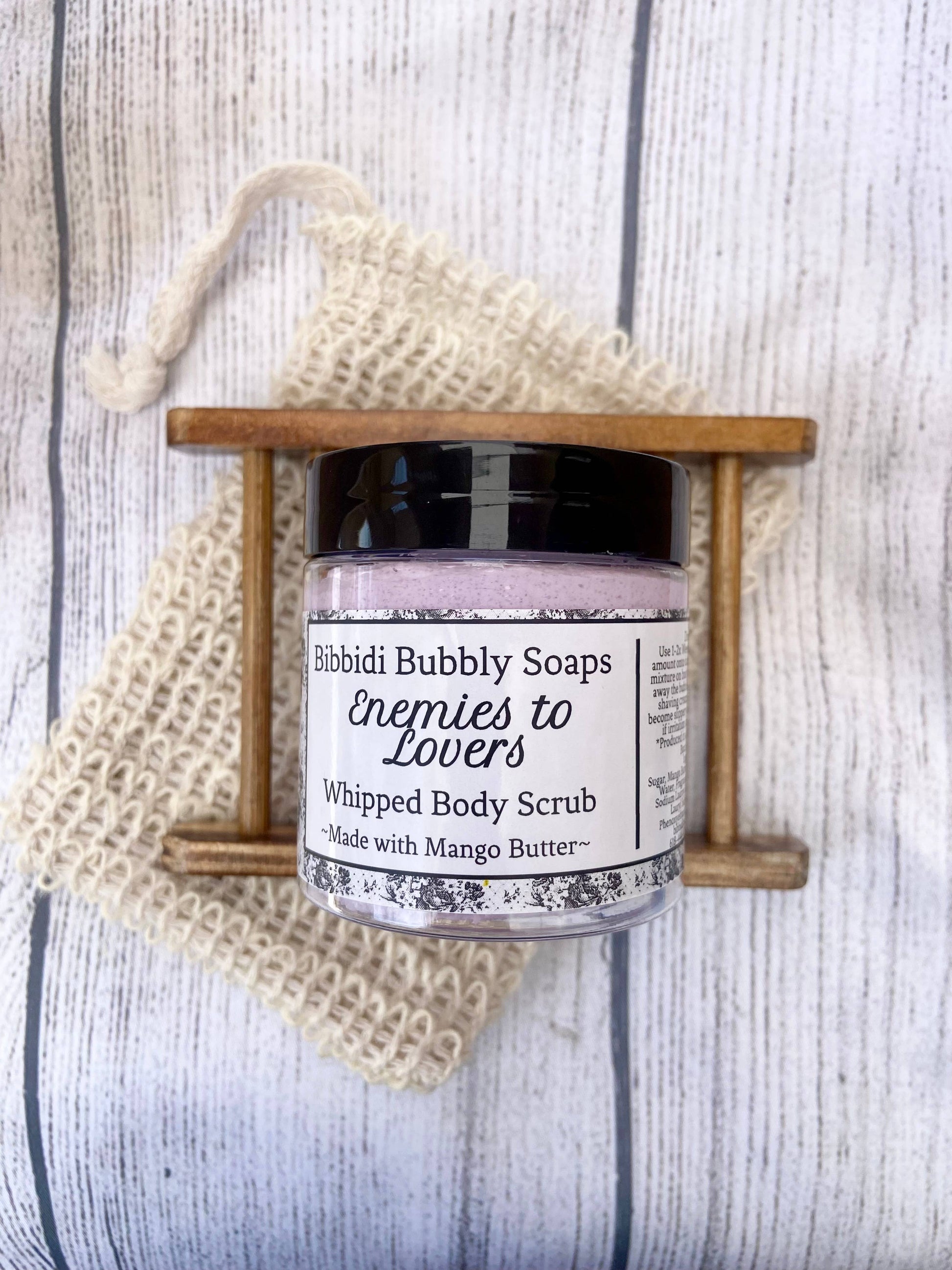 Jar of 'Enemies to Lovers' whipped body scrub by Bibbidi Bubbly Soaps on a wooden stand with a loofah.