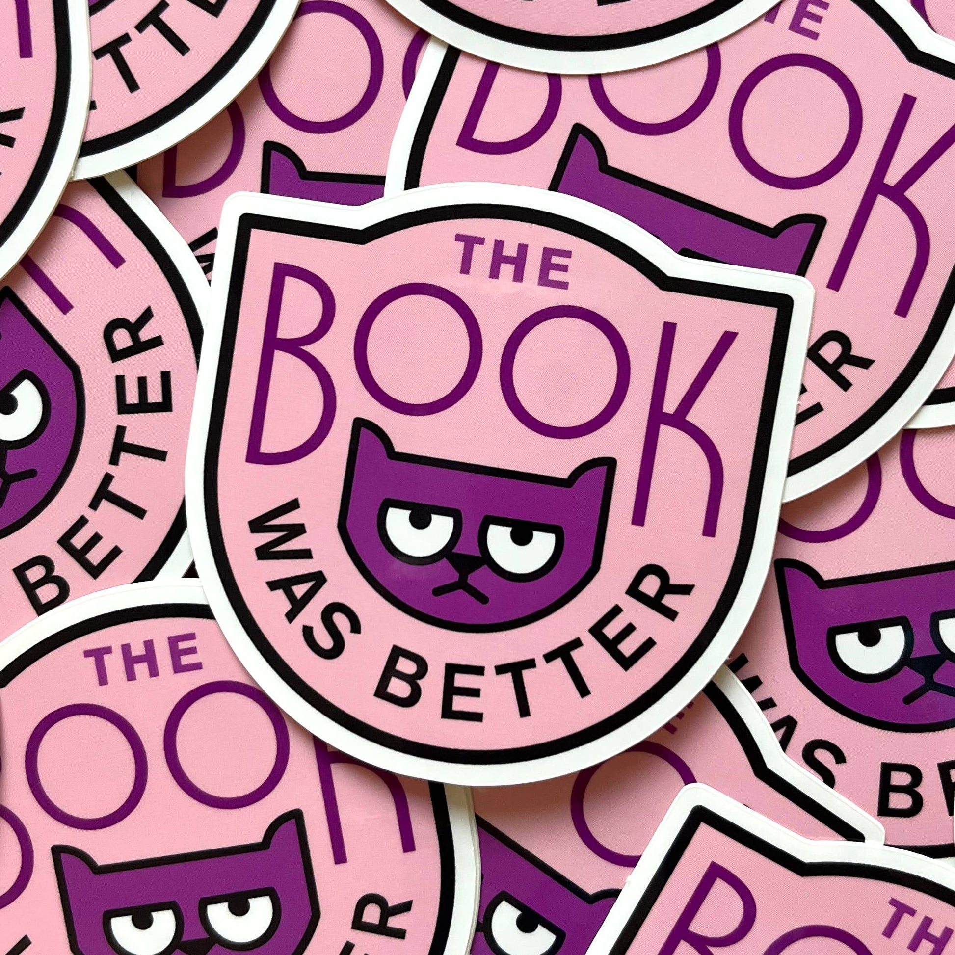 Stickers with a purple cat illustration and text 'The Book Was Better' on a pink background.