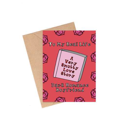 Greeting card with text 'To My Real Life, A Very Smutty Love Story, Dark Romance Boyfriend' on a red background with pink roses and a brown envelope.