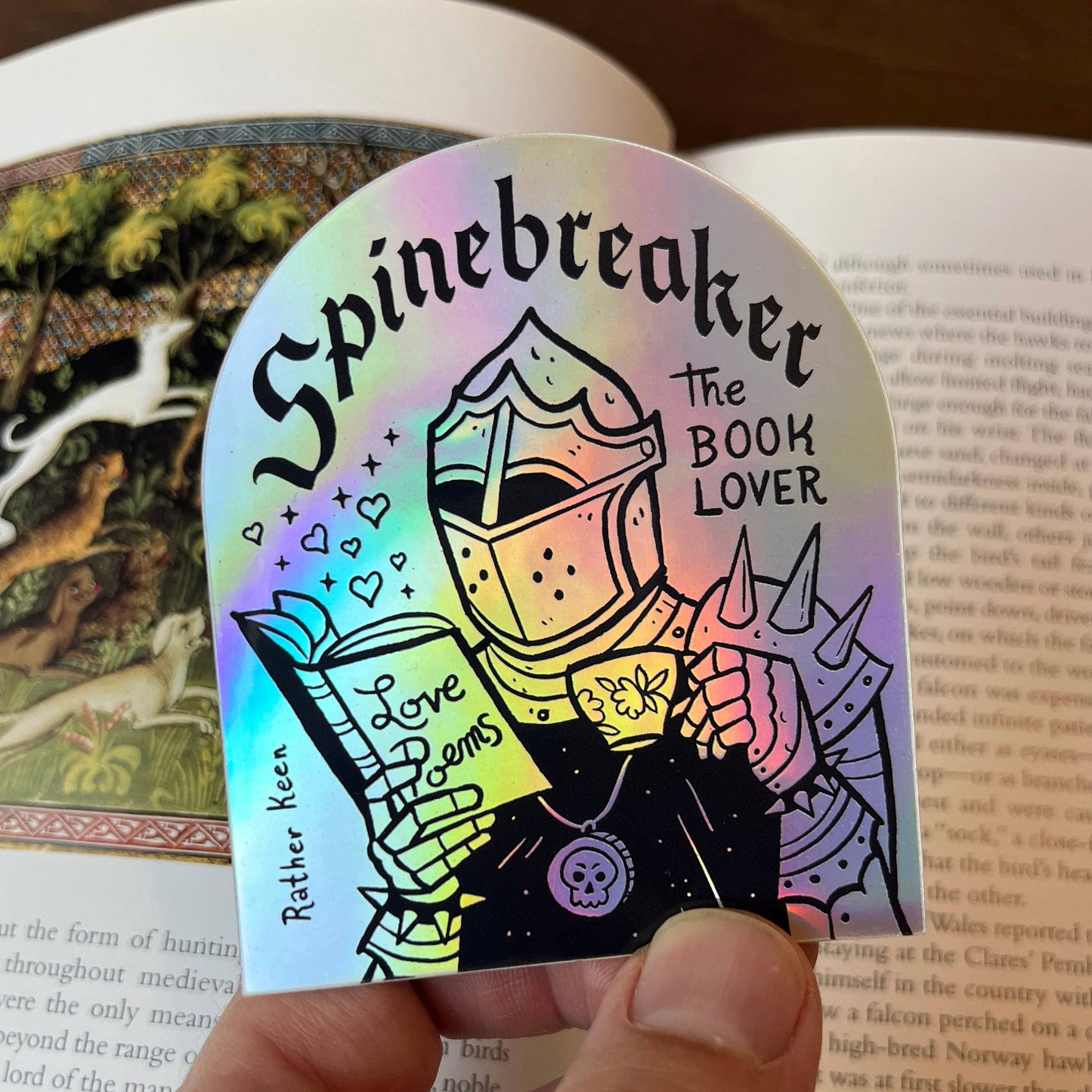 Holographic bookmark with 'Spinebreaker The Book Lover' design held over an open book.
