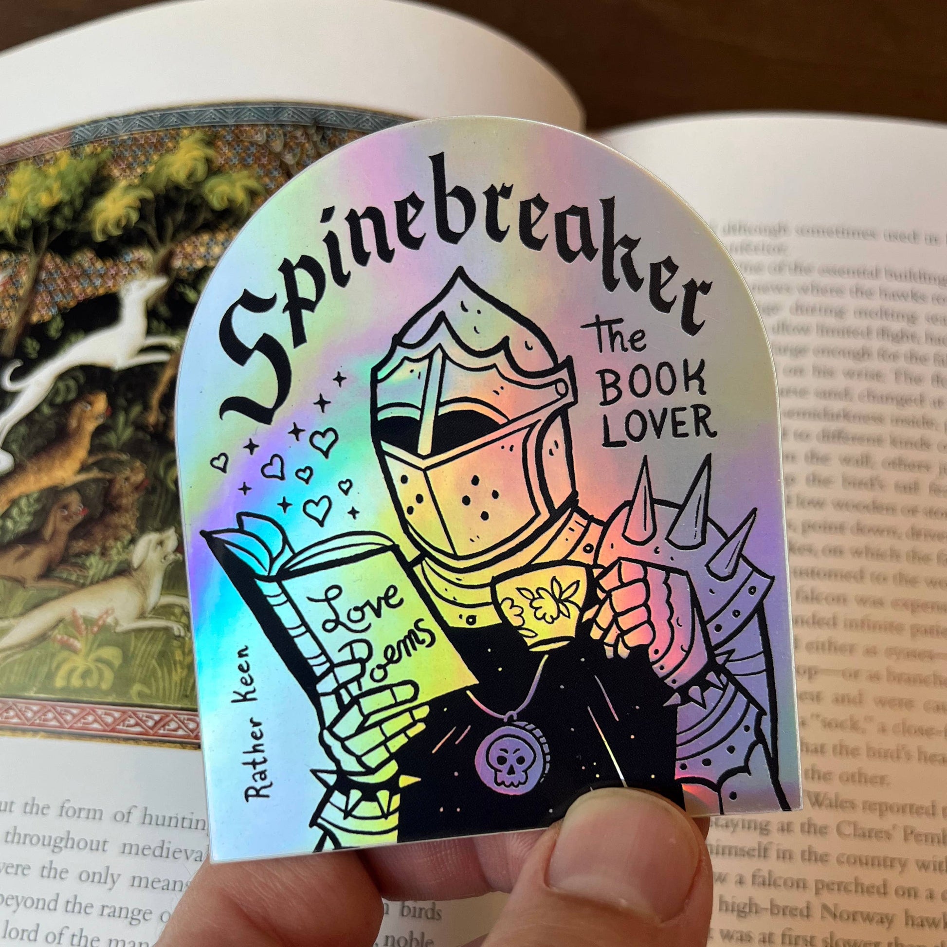 Holographic bookmark with 'Spinebreaker The Book Lover' design held over an open book.