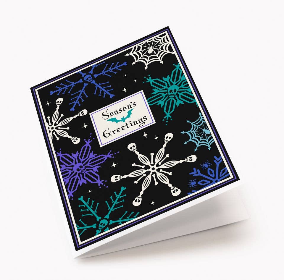 A square greeting card with a black background and seasonal winter motifs, including white snowflakes, purple and teal spiderwebs, and small white stars. A central white label reads 'Season's Greetings' with a teal bat graphic.