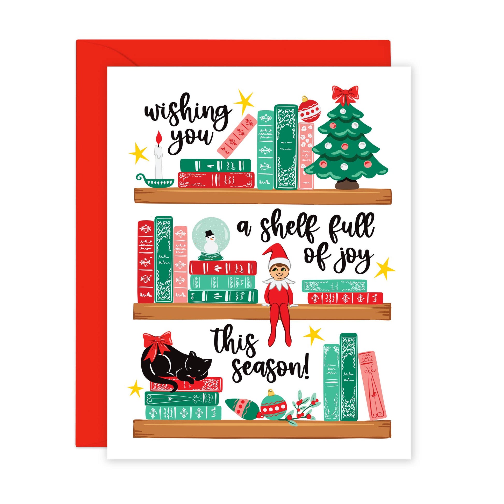 A Christmas greeting card with a white front featuring illustrated bookshelves, holiday books, a Christmas tree, an elf, a black cat, and festive text, shown with a red envelope behind it on a white background.