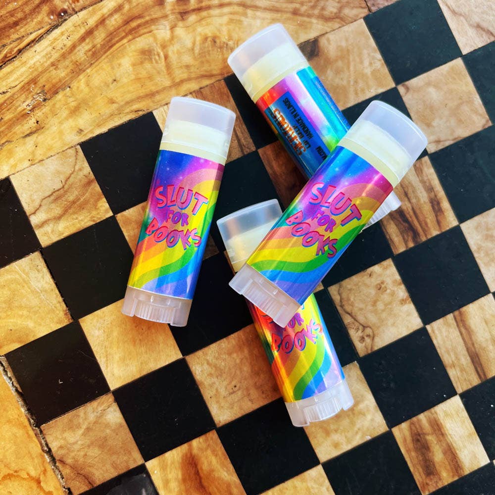 Four colorful lip balms with rainbow designs on a checkered wooden surface