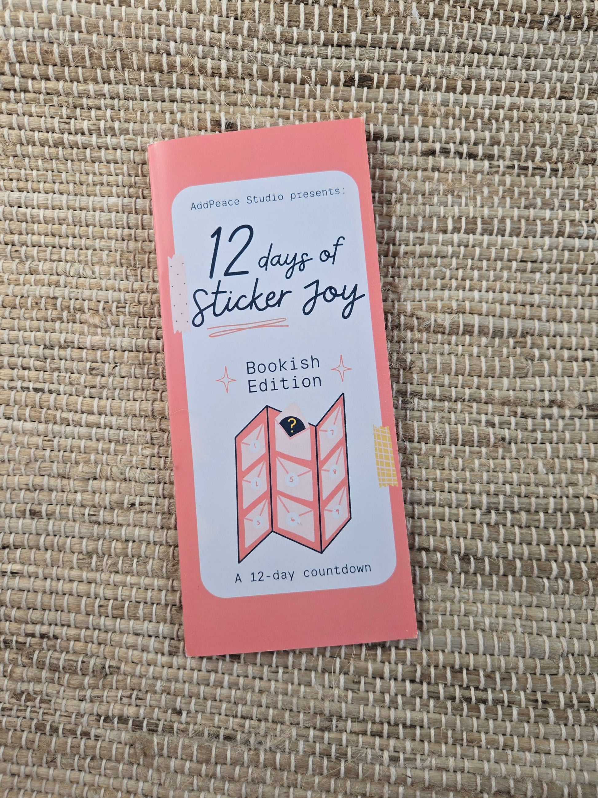 Pink packaging of '12 days of Sticker Joy' on a woven mat background