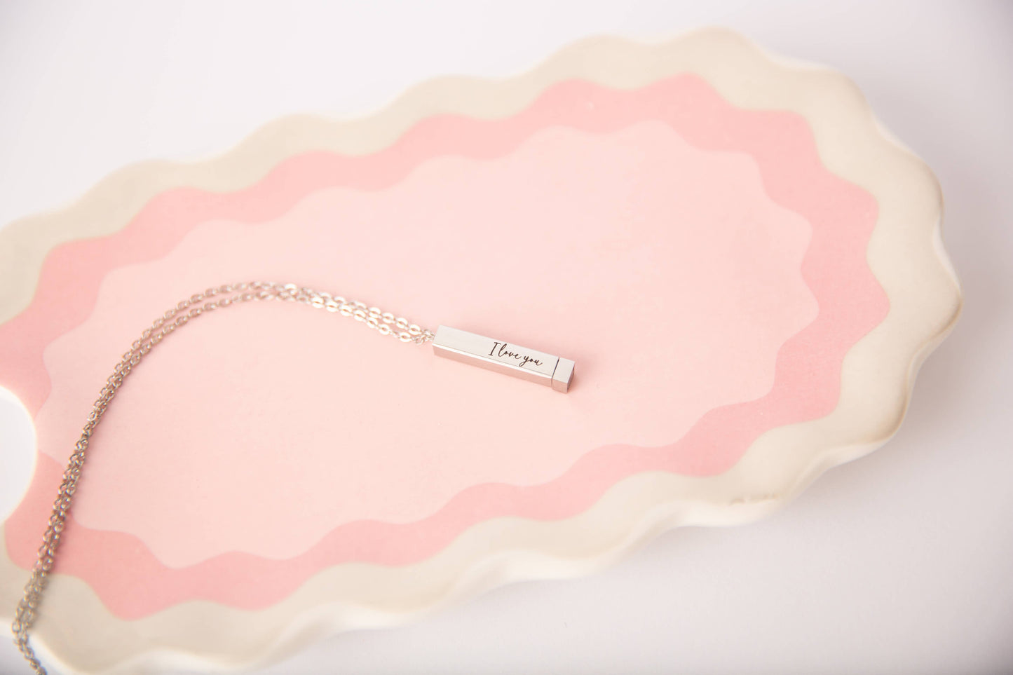 Necklace with 'I love you' pendant on a pink and white textured surface