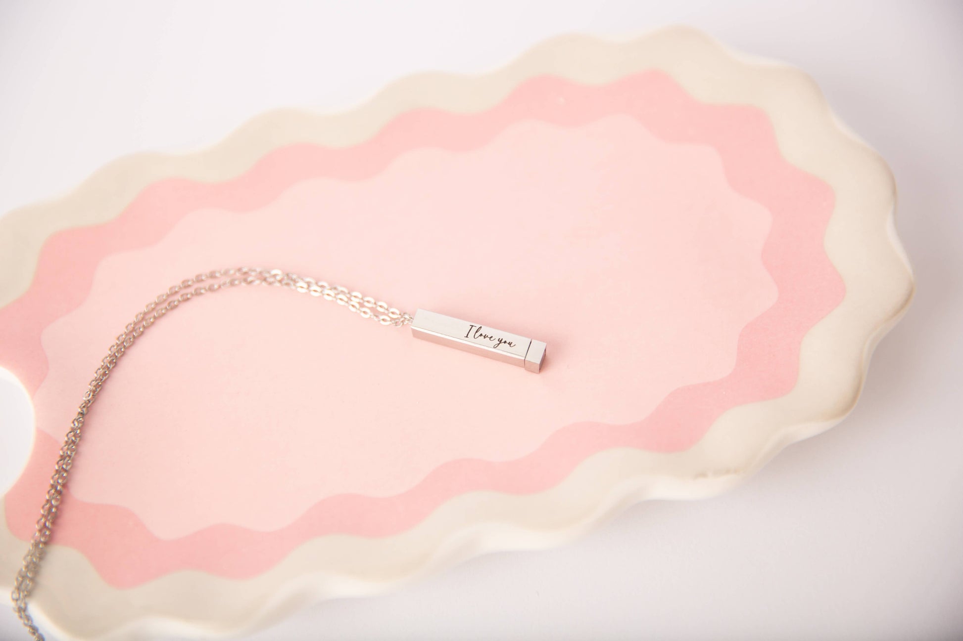 Necklace with 'I love you' pendant on a pink and white textured surface
