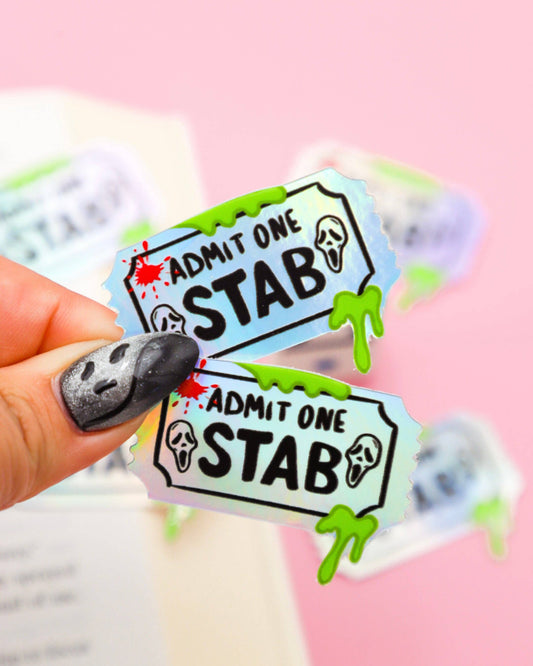 Two 'Admit One Stab' stickers held by a hand with a blurred background