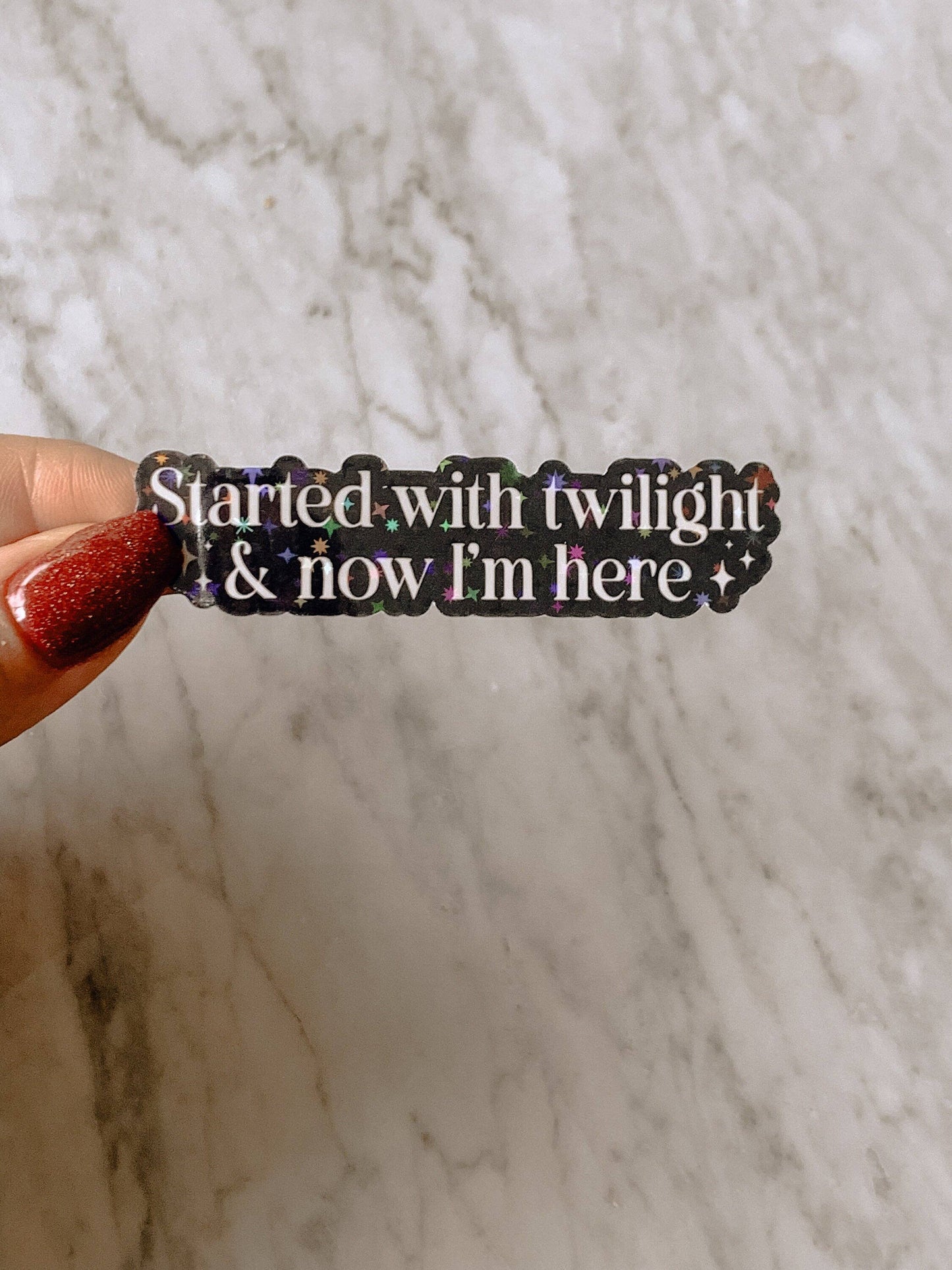 Sticker with text 'Started with twilight & now I'm here' held against a marble background