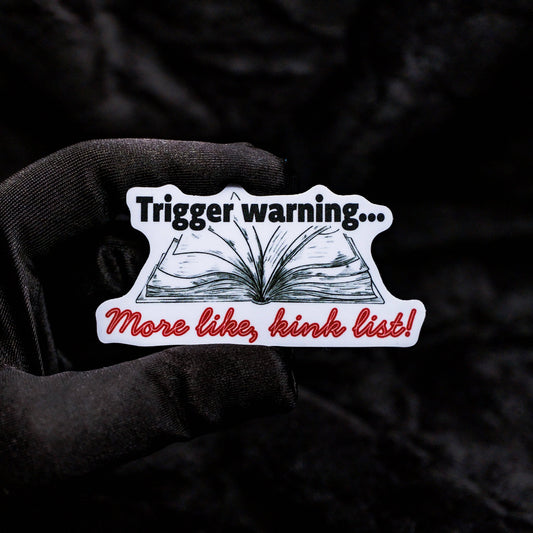 Sticker with text 'Trigger warning... More like, kink list!' held by a gloved hand against a dark background