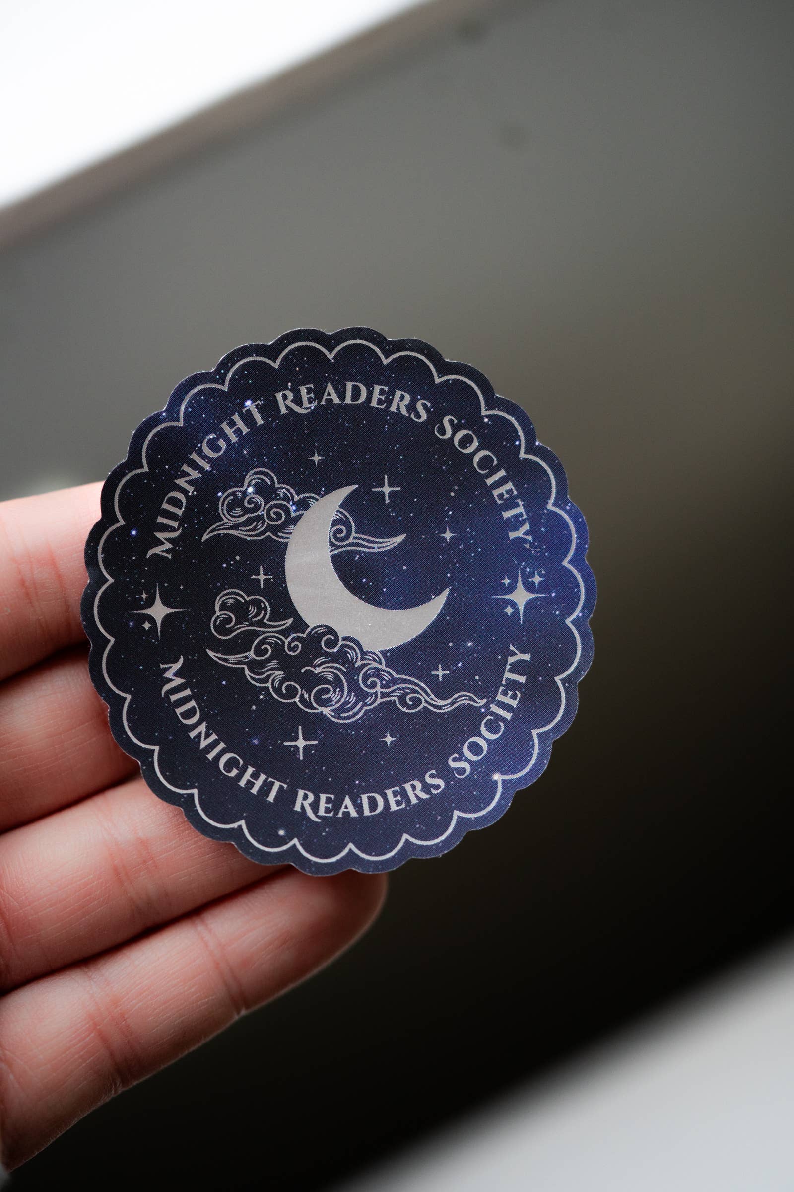 Sticker with 'Midnight Readers Society' design held over a dark surface