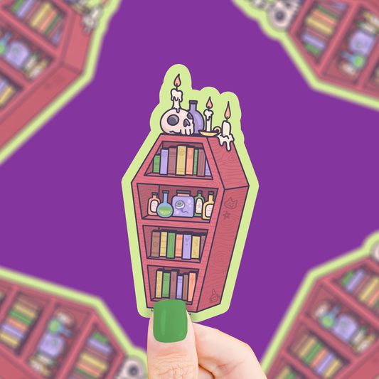 Hand holding a sticker of a bookshelf with books and candles against a purple background