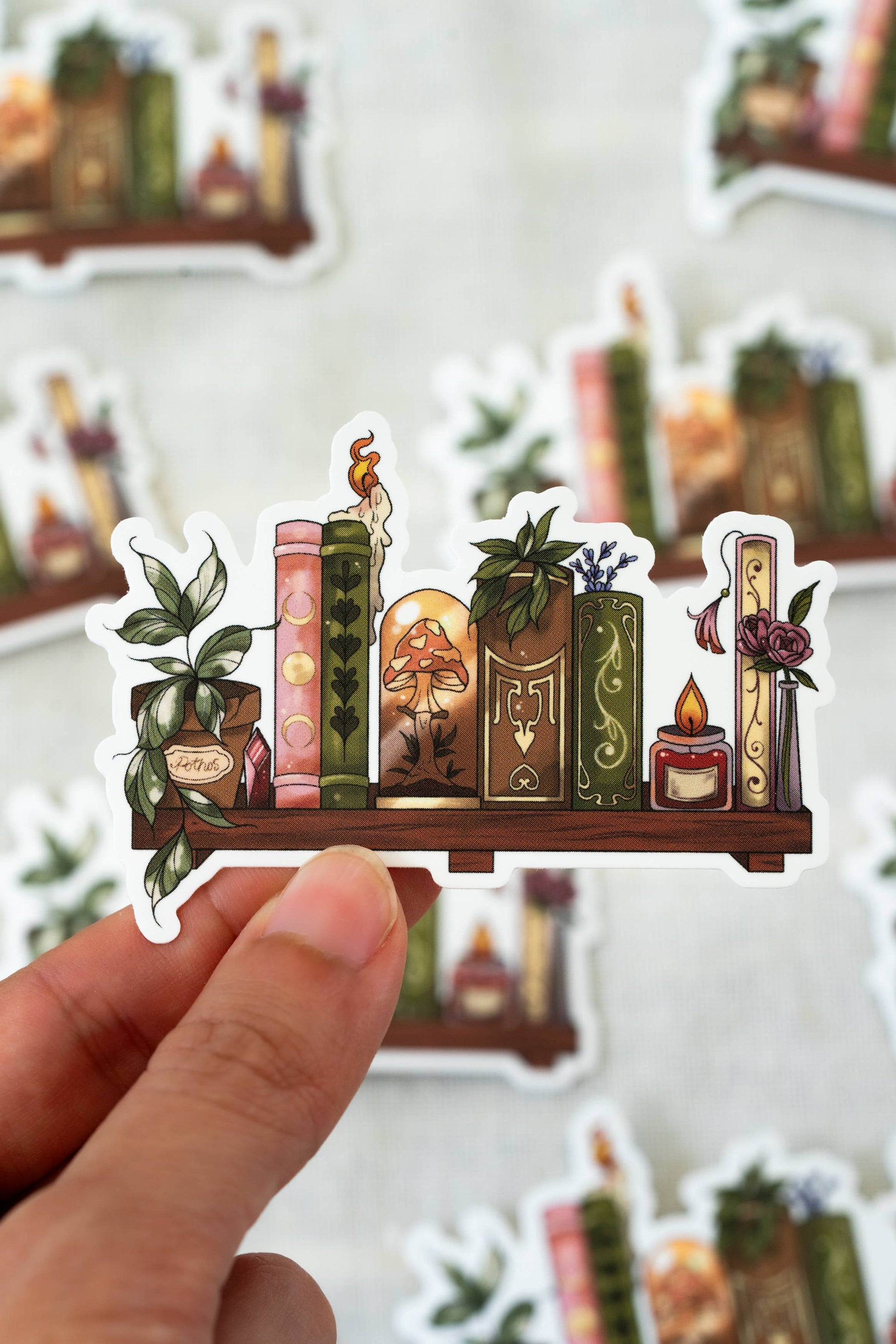 Sticker of a shelf with books, plants, and candles held by a hand against a blurred background.