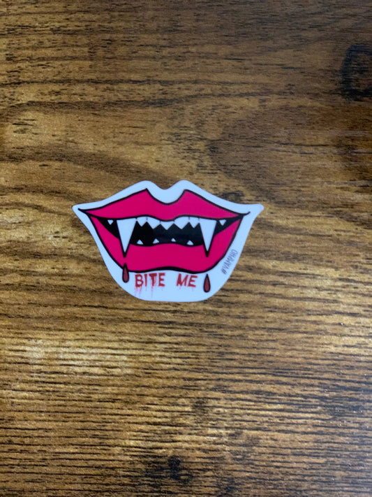 Sticker of a mouth with fangs and 'Bite Me' text on a wooden surface