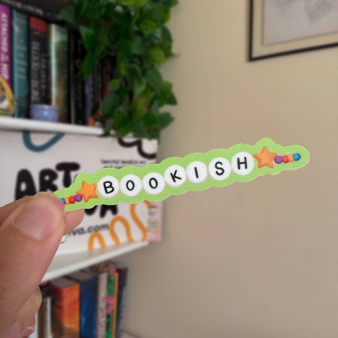 Hand holding a 'BOOKISH' decorative item with stars against a bookshelf background