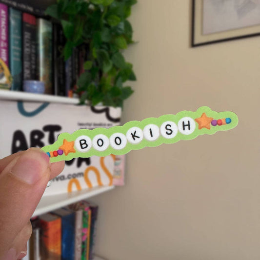 Hand holding a 'BOOKISH' decorative item with stars against a bookshelf background