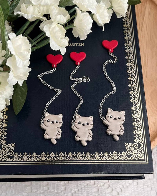 Cat-shaped chain bookmarks with red hearts on a decorative black and white surface with flowers.