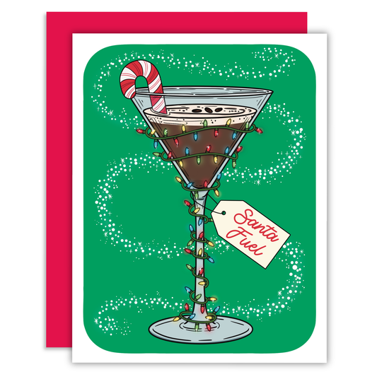 A festive greeting card featuring an illustrated martini glass filled with a dark drink, wrapped in holiday lights, with a candy cane on the rim and a tag reading 'Santa Fuel.' The card is shown with a bright pink envelope behind it on a white background.