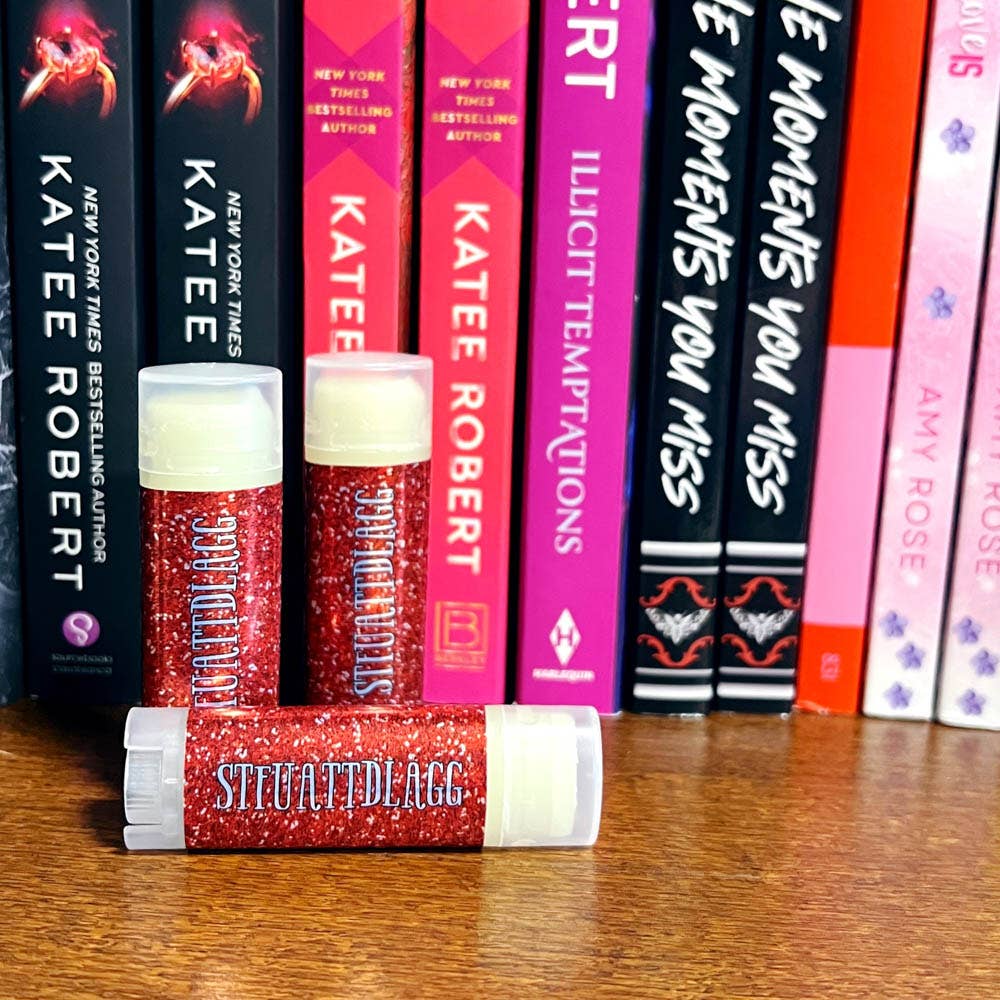 Red lip balm tubes with white caps on a wooden surface with books in the background