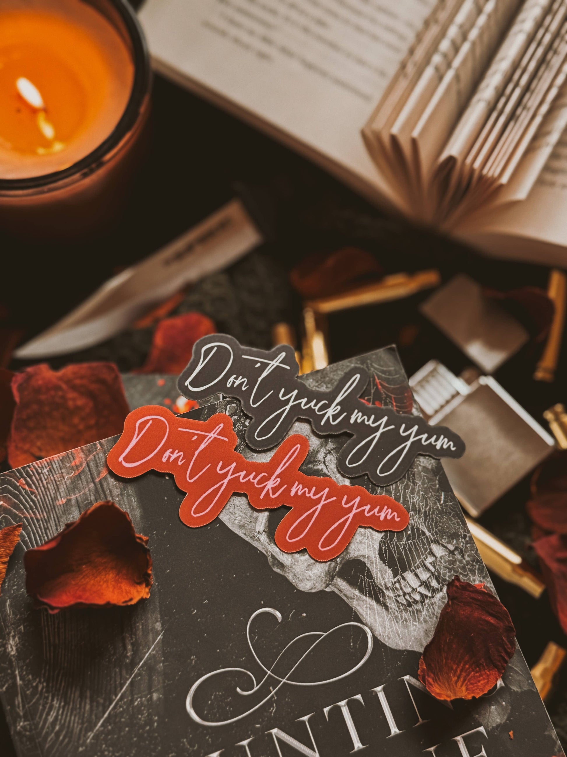 Book with 'Don't yuck my yum' stickers, candle, and red roses on a dark surface