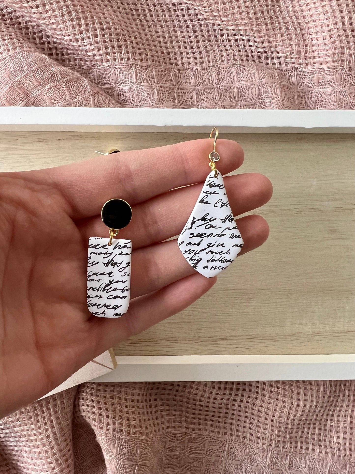 Hand holding two earrings with black and white designs against a neutral background