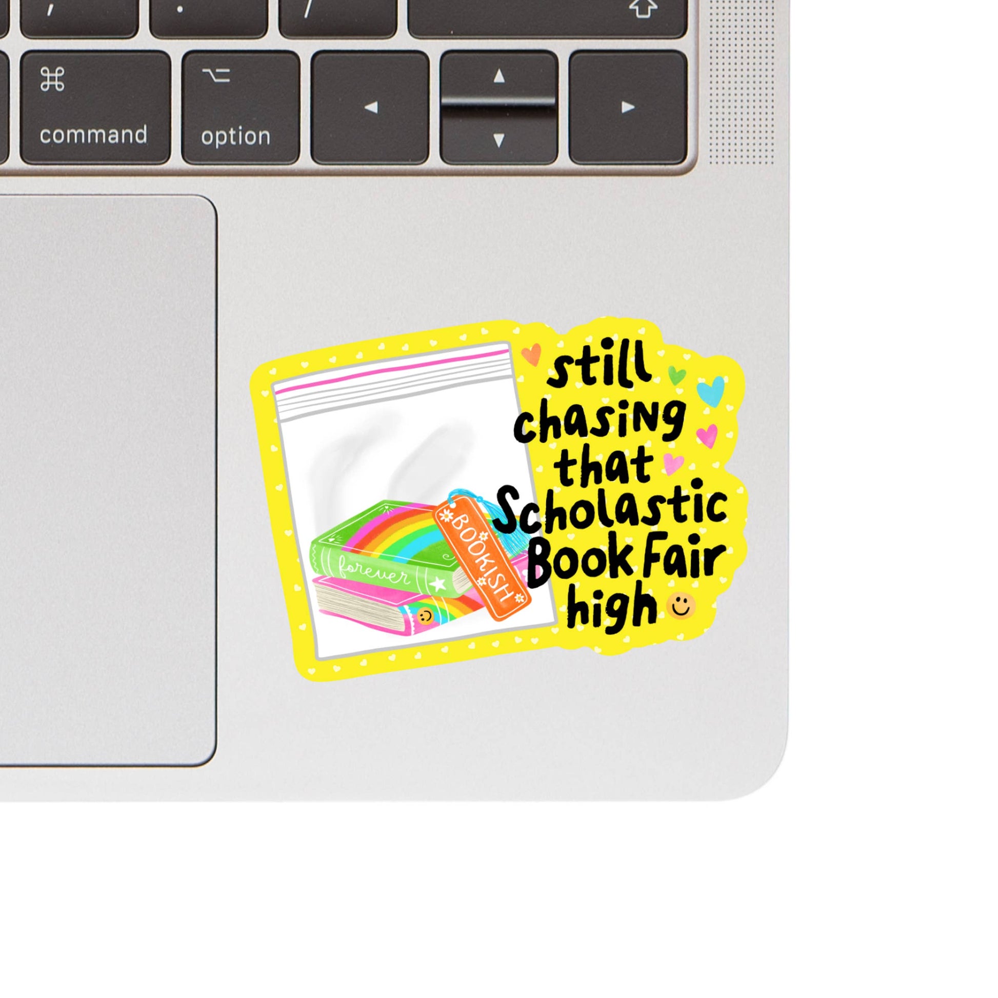 Laptop with a colorful sticker reading 'still chasing that Scholastic Book Fair high' on a white background