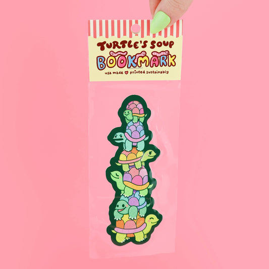 Colorful turtle-shaped bookmark in packaging with 'Turtle's Soup' branding on a pink background
