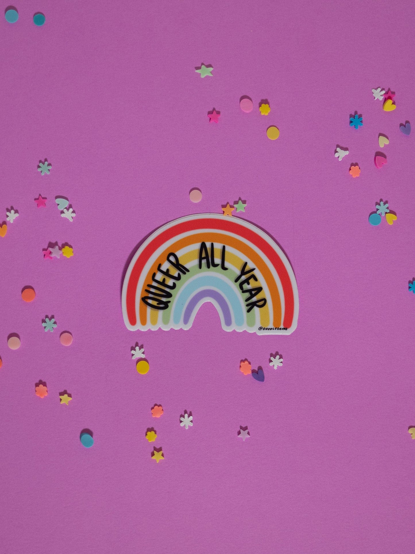 Rainbow sticker with 'Queer All Year' text on a purple background with confetti